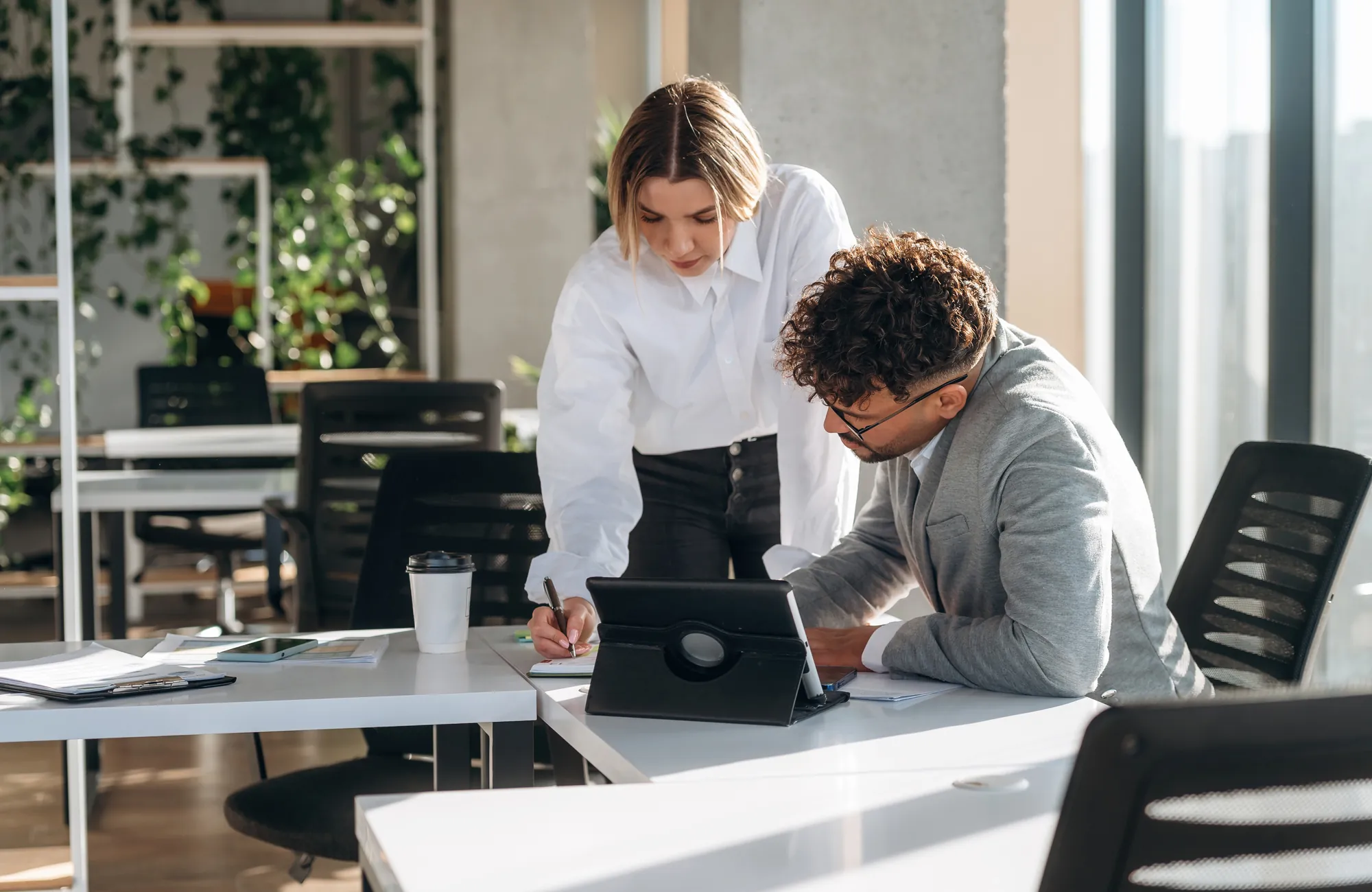 Two colleagues reviewing a tablet together at a desk in a bright office