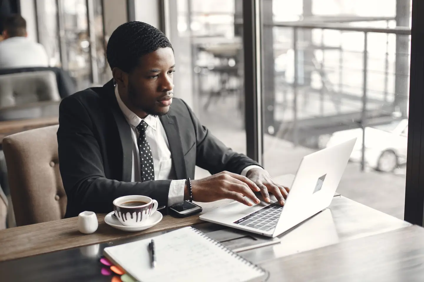 Man in a Suit Sitting at a Table in a Cafe and Using Laptop